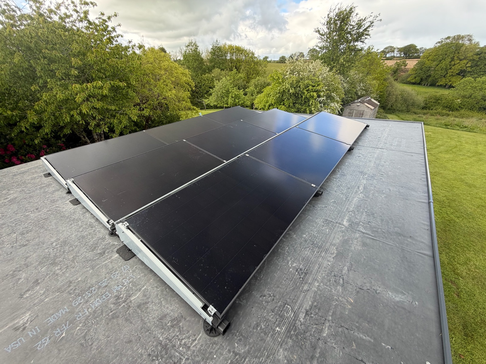 Panels on ballasted frames across a flat roof, with open countryside behind.