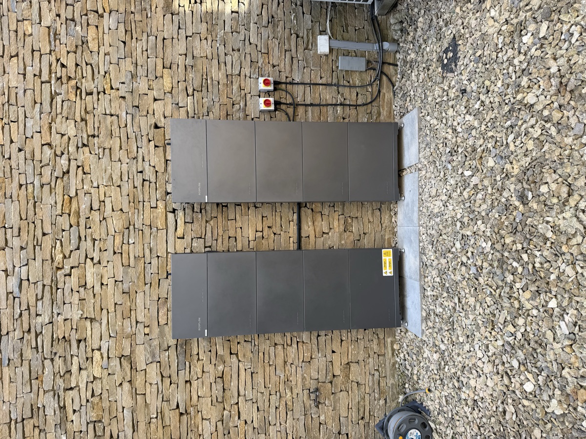 Two floor-standing home batteries mounted against a dry stone wall, cabled back into the house.