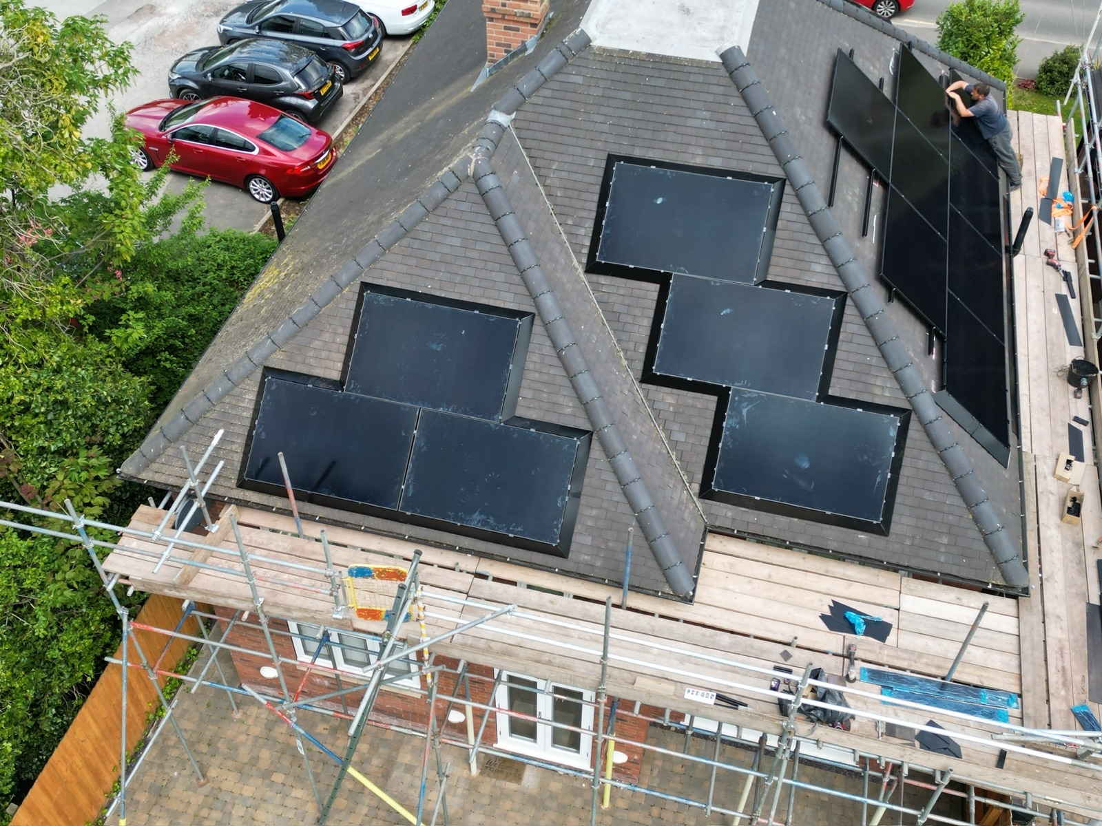 An installer setting panels into a slate roof mid-installation, with scaffold up around the house.