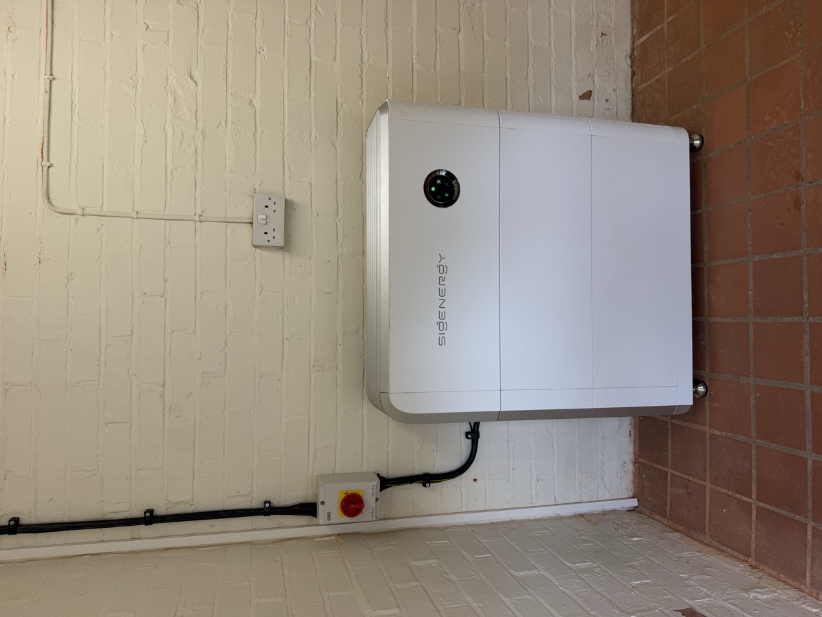 A Sigenergy SigenStor battery standing in a garage against a painted brick wall.