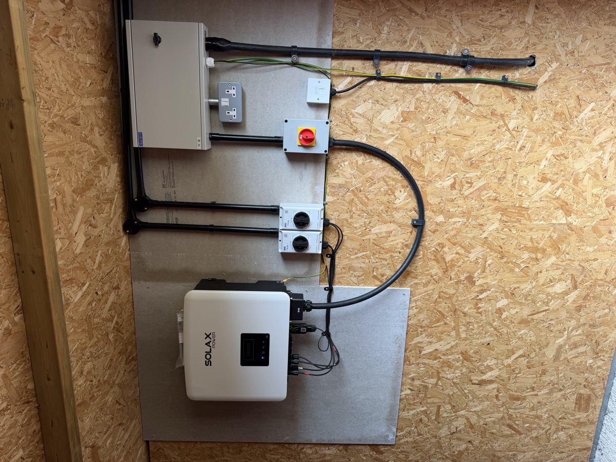 A wall-mounted SolaX inverter on a commercial installation, with isolators, consumer unit and cable runs all clipped and squared off.